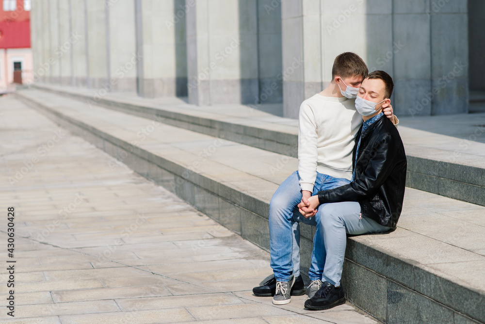 Young gay couple wearing medical mask, hugging and kissing at the city. Young gay couple wearing medical mask, hugging and kissing at the city.
