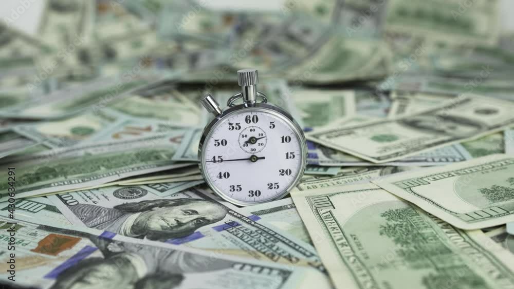 American dollars falling from above on an old vintage stopwatch. Time is money. The concept of investment, bank deposits, financial savings. American dollars falling from above on an old vintage stopwatch. Time is money. The concept of investment, bank deposits, financial savings.