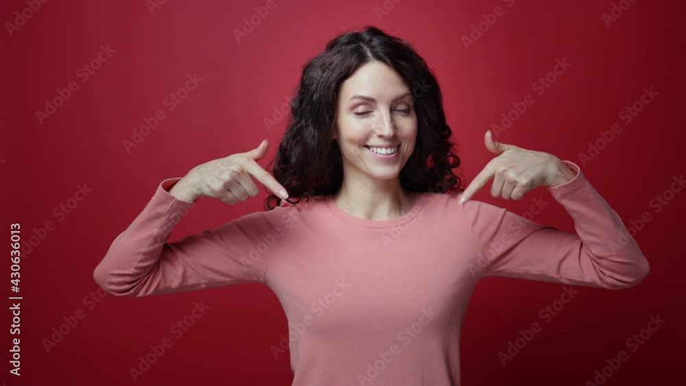 Happy smiling brunette woman point fingers down, actively recommend to subscribe, follow or press like button under video. Closeup portrait of cheerful female show advertising area over red background