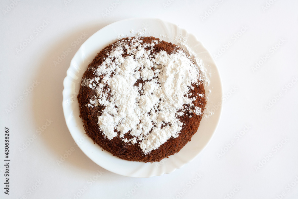 Chocolate sponge cake with powdered sugar on a plate, isolated on a white background