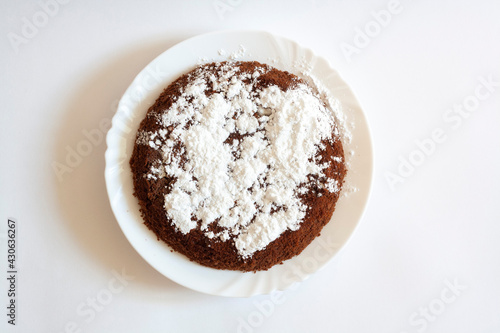 Chocolate sponge cake with powdered sugar on a plate, isolated on a white background