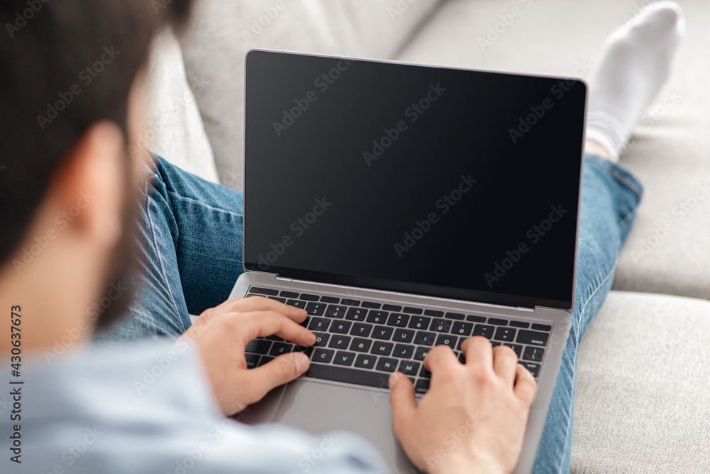 Technology concept. Unrecognizable guy using laptop computer with blank screen, mockup, selective focus Technology concept. Unrecognizable guy using laptop computer with blank screen, mockup, selective focus