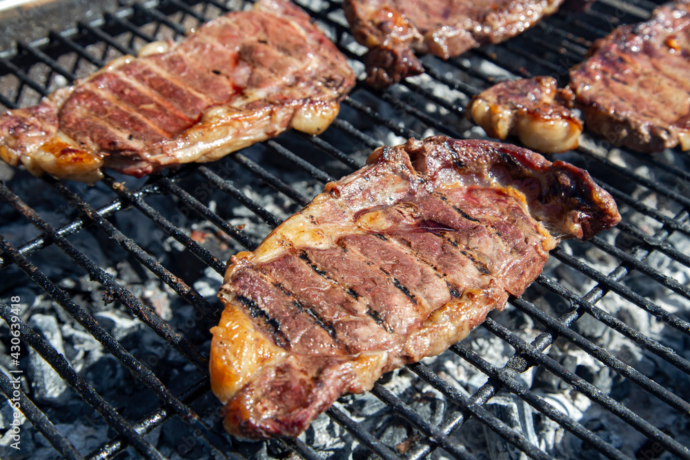 Fresh beef steaks being fried or prepared on grill or BBQ with pepper, spices and seasoning, delicious food.