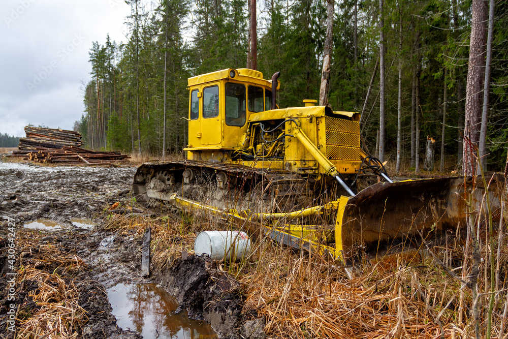 Logging in the forest. Yellow tracked forestry tractor. Dirty forest road, logs in the background. Logging in the forest. Yellow tracked forestry tractor. Dirty forest road, logs in the background.