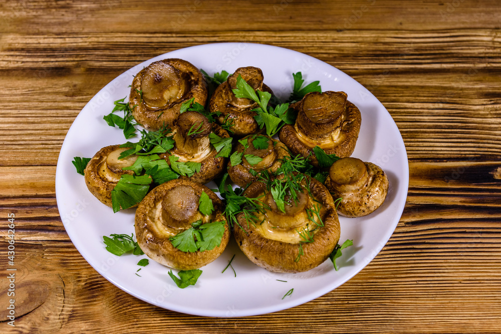 Plate with baked champignons, dill and parsley on a wooden table Plate with baked champignons, dill and parsley on a wooden table