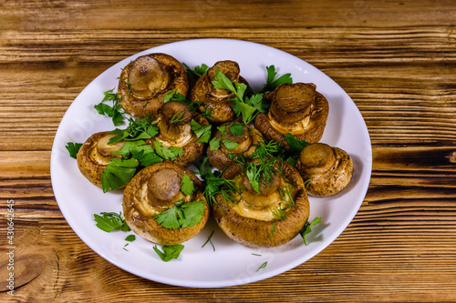 Plate with baked champignons, dill and parsley on a wooden table