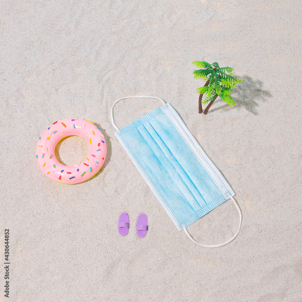 Summer scene on the beach during the virus. Sunbathing on the beach. Pandemic mask. Pink rubber for swimming, slippers and palm tree. Summer scene on the beach during the virus. Sunbathing on the beach. Pandemic mask. Pink rubber for swimming, slippers and palm tree.