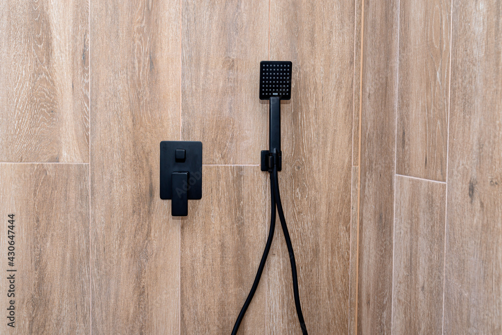 Black, matte hand shower mounted on a tiled wall, imitating wood. Black, matte hand shower mounted on a tiled wall, imitating wood.