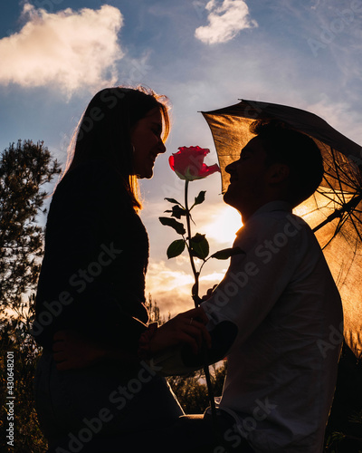 silhouette of a couple with a umbrella in a sunset with a rose