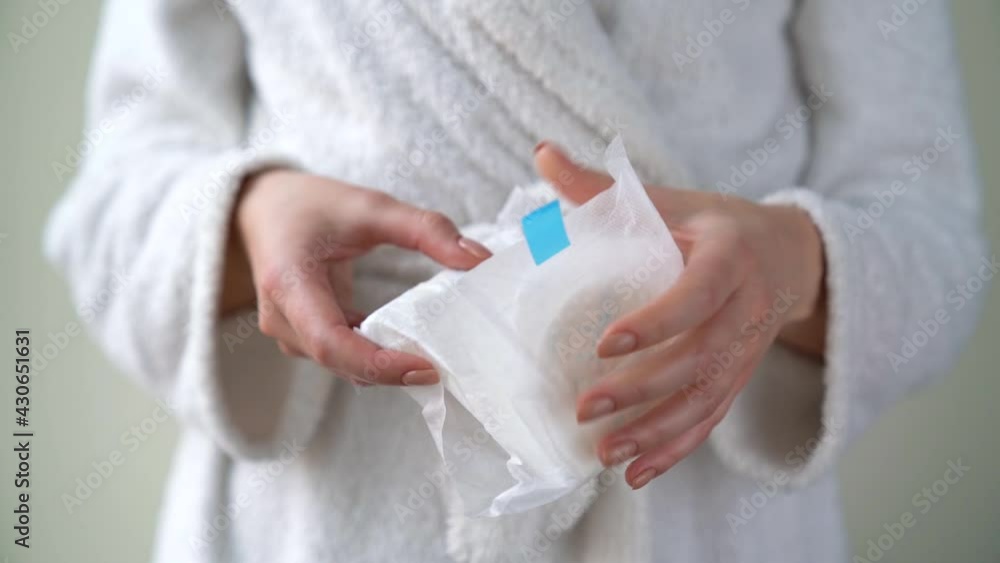 Closeup female hand is holding sanitary cotton pad, napkin, towel. Woman is going to use product for absorbing menstrual blood. Critical days and women health concept. Personal hygiene and care. Closeup female hand is holding sanitary cotton pad, napkin, towel. Woman is going to use product for absorbing menstrual blood. Critical days and women health concept. Personal hygiene and care.