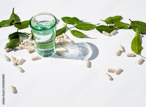 A glass of water. Capsules are scattered and green leaves. Alternative medicine and nutraceutical topics. Copy space for text.