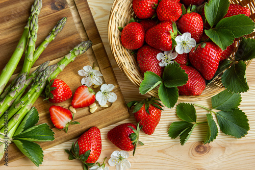 fresh season strawberries and green asparagus mit strawberries flowers, straw basket, wooden cutting board, wooden background, summer, June,  spring time, uncooked, fresh strawberries, fruit