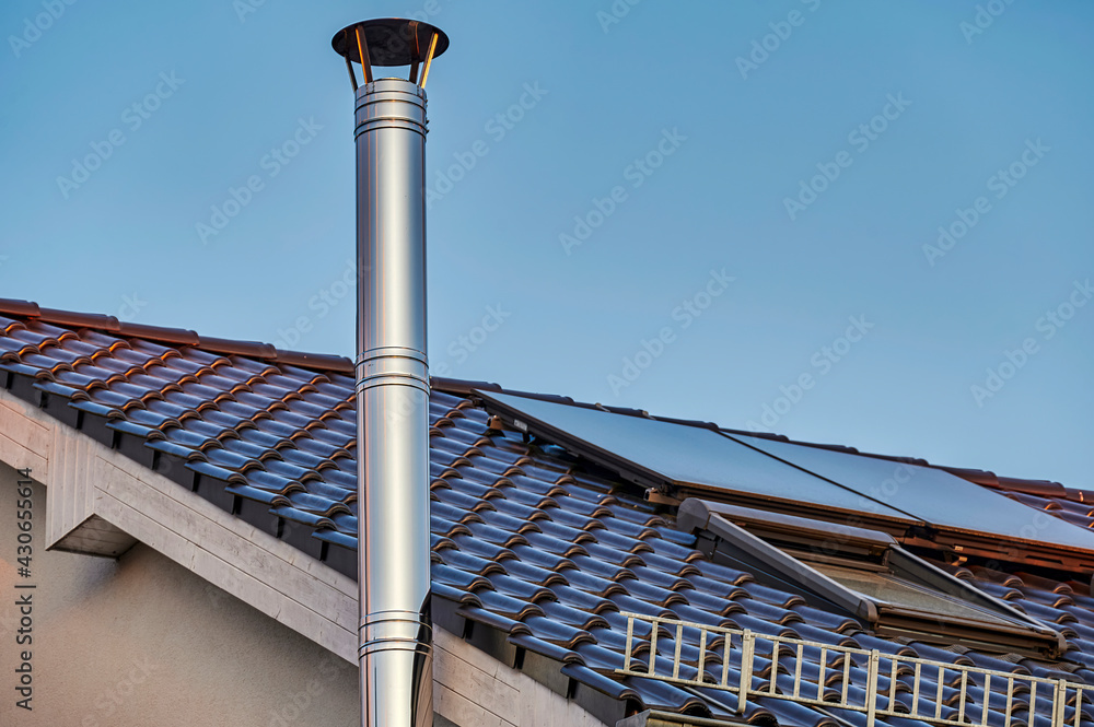 A stainless steel chimney and parts of a roof with solar panels at dusk ...