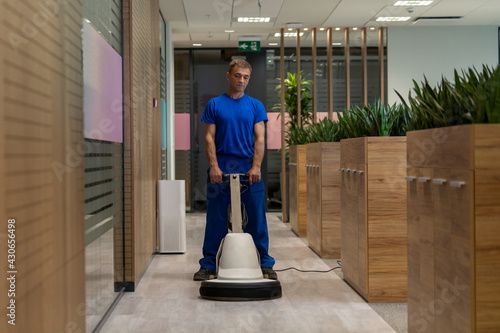 Cleaning worker in a blue uniform polishing floor in an office