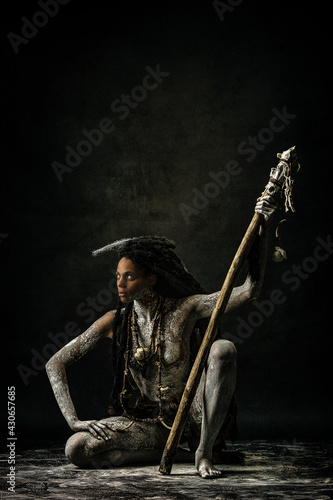 Tribal shaman covered in clay, wearing dreadlocks, bone necklaces and a scepter