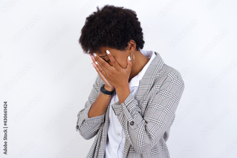 Sad African American businesswoman with curly bushy hair wears formal clothes over white background crying covering her face with her hands. Sad African American businesswoman with curly bushy hair wears formal clothes over white background crying covering her face with her hands.