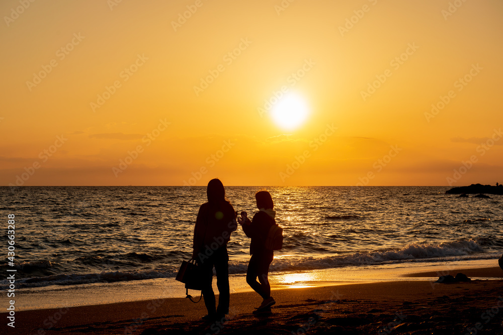 海に沈む夕日を眺める2人の若い女性のシルエット　秋谷海岸　