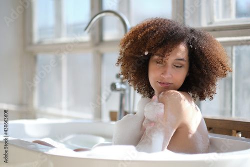 Fotografia, Obraz Smiling and relaxing african american woman bathing in a tub full of foam