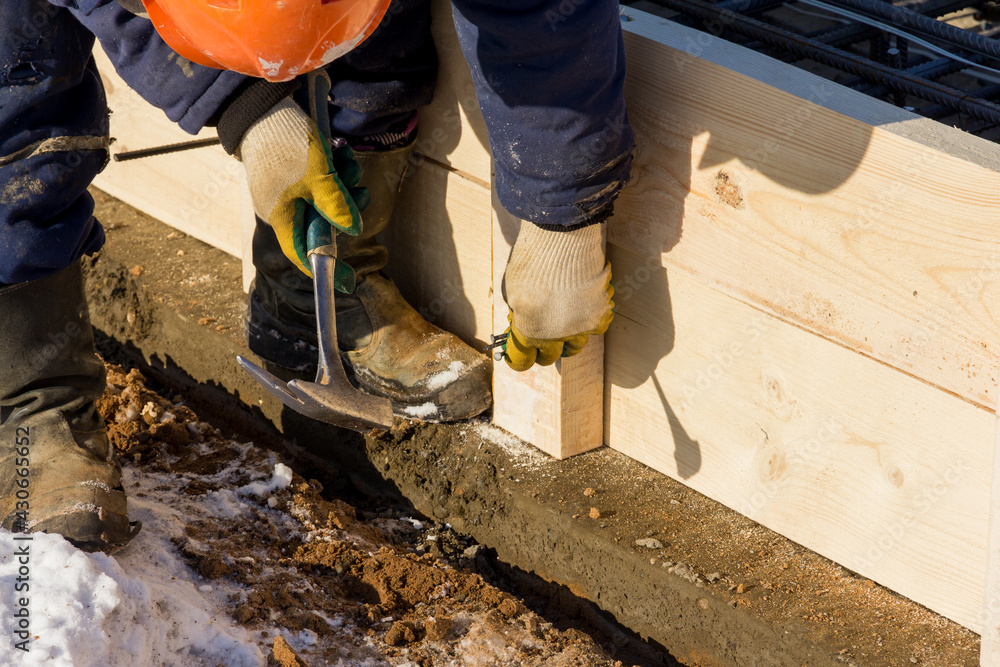 A worker hammers a nail at a construction site. Installation of wooden formwork. construction work A worker hammers a nail at a construction site. Installation of wooden formwork. construction work