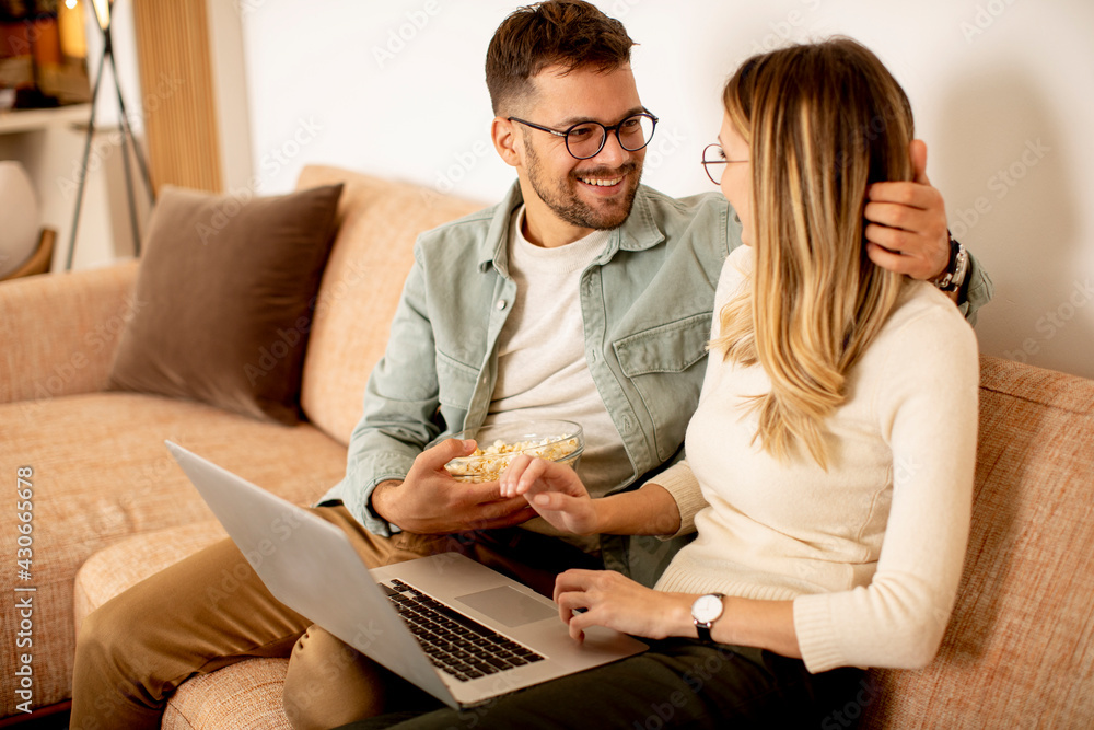 Young couple using laptop together while sitting on sofa at home Young couple using laptop together while sitting on sofa at home