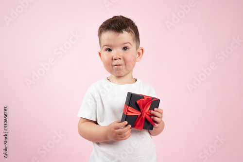 Cute boy in white t-shirt holding black box gift in front, fpink background, Valentines day, mother's day. photo