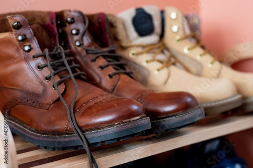 A close up of men’s brown brogue lace up boots on a wooden shoe rack with intentional selective focus, shallow depth of field and bokeh.