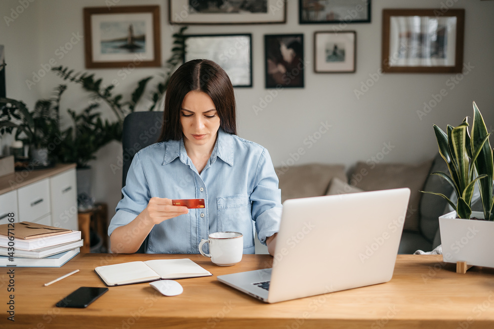 Happy smiling woman shopping online. Joyful brunette holds credit card, makes online purchases, online payments using laptop, sitting in living room Happy smiling woman shopping online. Joyful brunette holds credit card, makes online purchases, online payments using laptop, sitting in living room