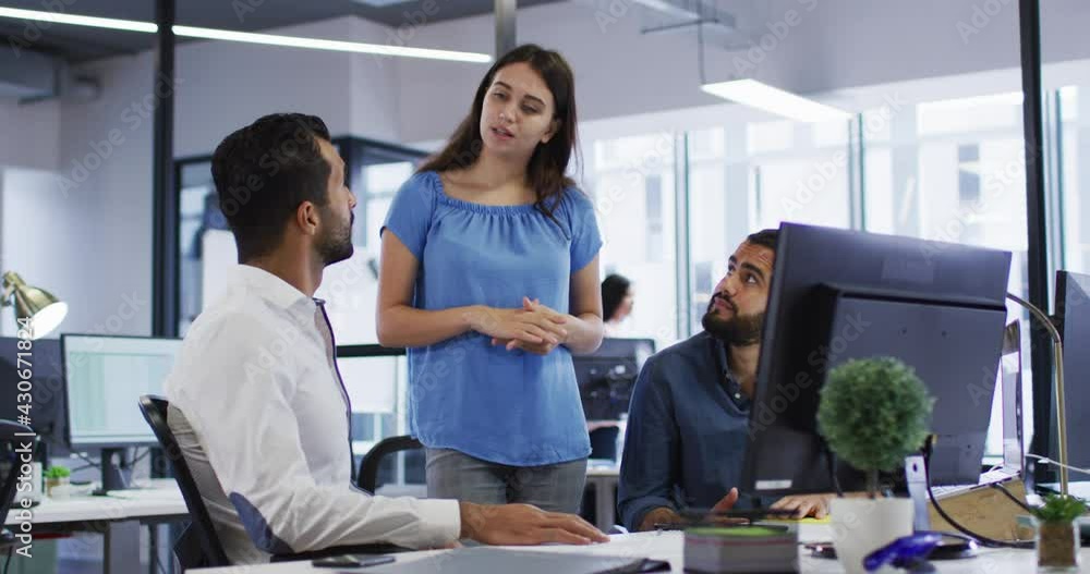 Caucasian businesswoman standing in discussion with two mixed race male colleagues at their desk