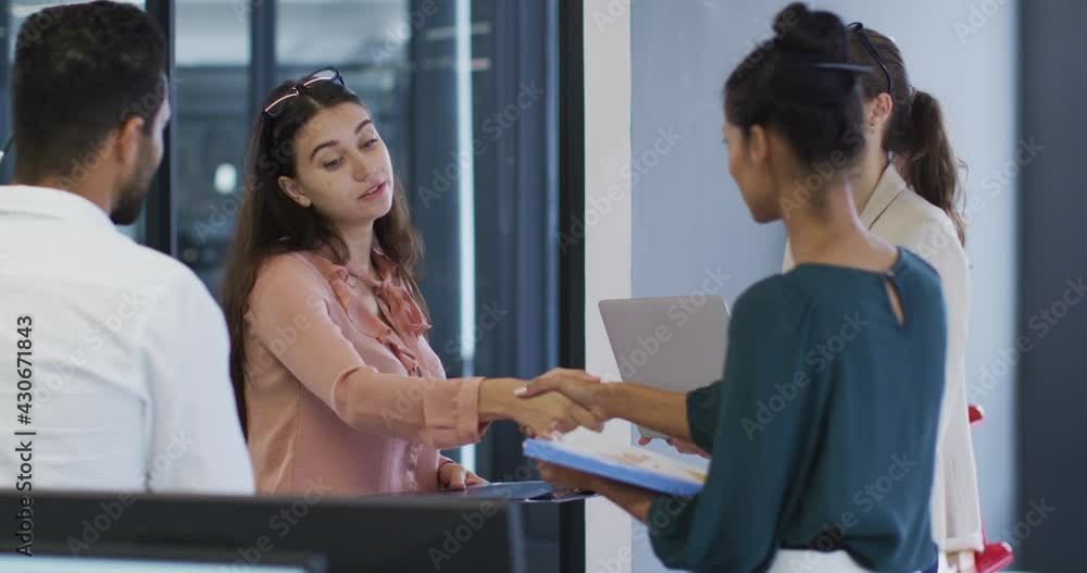 Two diverse businesswomen standing shaking hands during meeting with colleagues Two diverse businesswomen standing shaking hands during meeting with colleagues