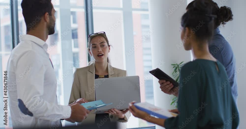 Caucasian businesswoman holding laptop talking to diverse colleagues standing at office meeting Caucasian businesswoman holding laptop talking to diverse colleagues standing at office meeting