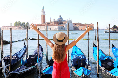 Holidays in Venice. Back view of beautiful girl with raised arms up enjoying view of Venice Lagoon with the island of San Giorgio Maggiore and gondolas moored. © zigres