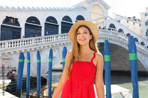 Beautiful young woman with a red dress is standing in front of the famous Rialto Bridge in Venice, Italy
