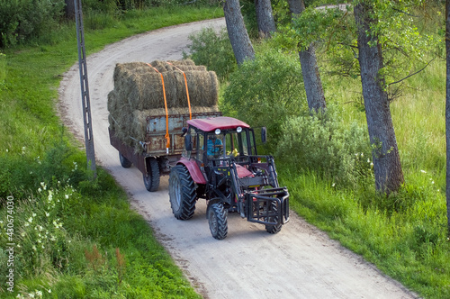 Traktor ciągnik przewożący bele siana po wiejskiej drodze