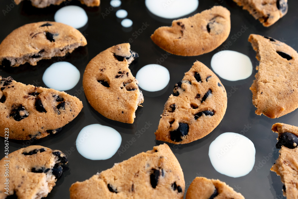 Pieces of chocolate chip cookies with milk drops on black background. Delicious cookies with chocolate crumbs. Pieces of chocolate chip cookies with milk drops on black background. Delicious cookies with chocolate crumbs.