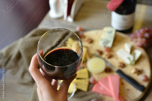 glasse of red wine in the hand, cheese plate on background, party invitation template with free space for text