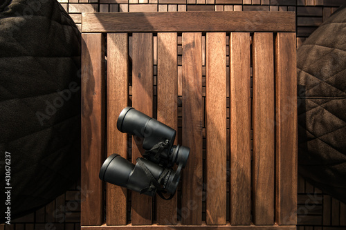 Black binoculars on a brown wooden table background with copy space