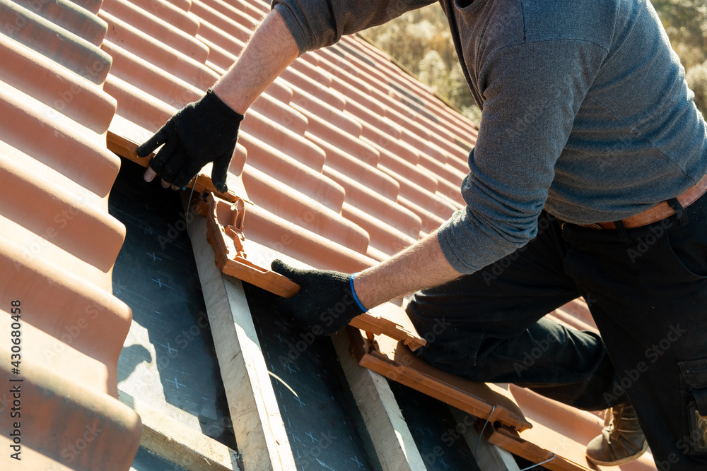 Φωτογραφία Closeup of worker hands installing yellow ceramic roofing tiles mounted on wooden boards covering residential building roof under construction