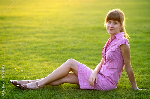 Side view of young cute woman sitting on grass in good weather. Concept of resting on fresh air on nature.