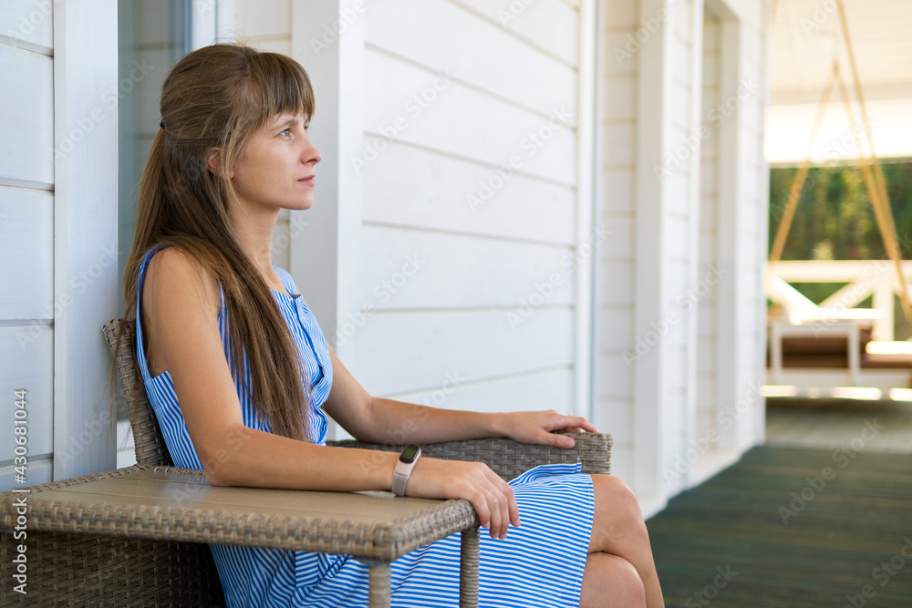 Side view of young beautiful woman resting on fresh air sitting on porch at home. Concept of enjoying nature with good weather.
