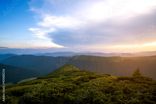 Summer evening mountain landscape with grassy hills and distant peaks at colorful sunset.