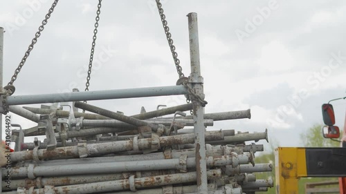 Crane unloading mechanism with chains and hooks. Unloading reinforcement pipes by crane.