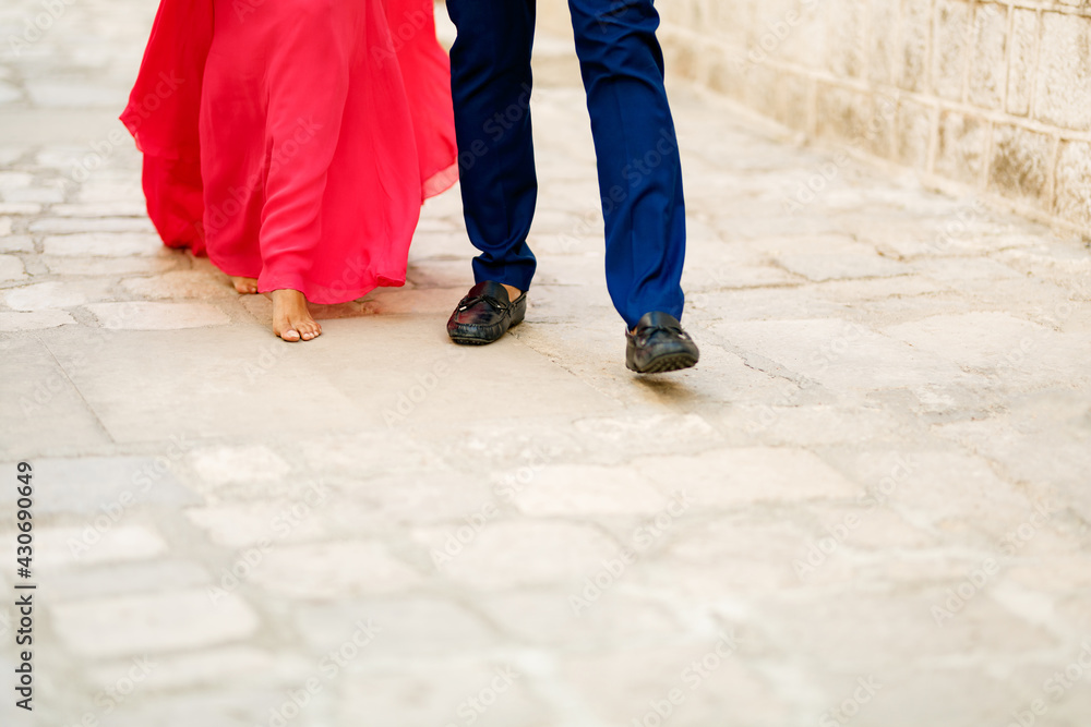 Barefoot bride in a long bright pink dress and the groom walking along a cobbled road, close-up