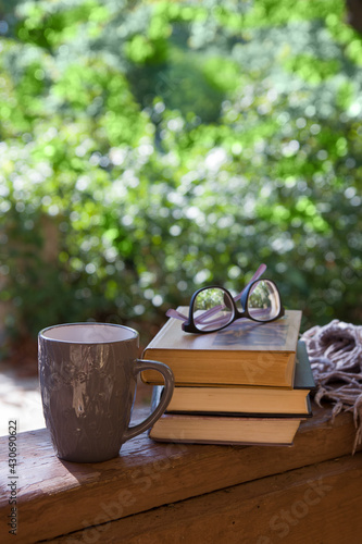Books with a cup and glasses on the porch of the house against the backdrop of greenery. Summer or spring leisure concept