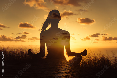 Young woman mediating facing the sunset sky. Double exposure photo