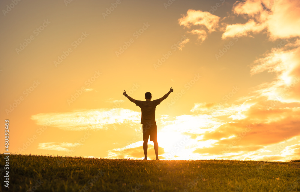 Feeling positive and happiness. Young man standing facing the sunrise with thumbs up to the sky. 
