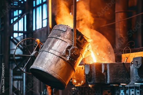 Fotografija Metal casting process in foundry, liquid metal pouring from container to mold with clubs of steam and sparks, heavy metallurgy industry background