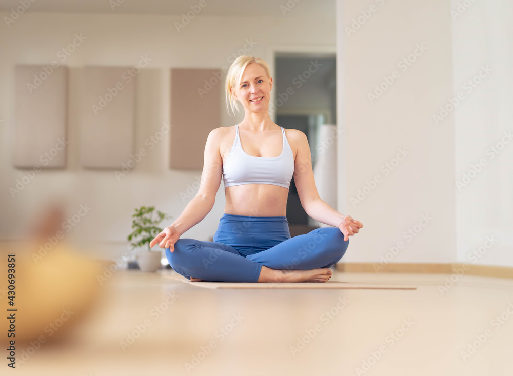 Young woman stretches, after a yoga session, in her empty studio, closed for the corona virus. Looks at the camera smiling Young woman stretches, after a yoga session, in her empty studio, closed for the corona virus. Looks at the camera smiling
