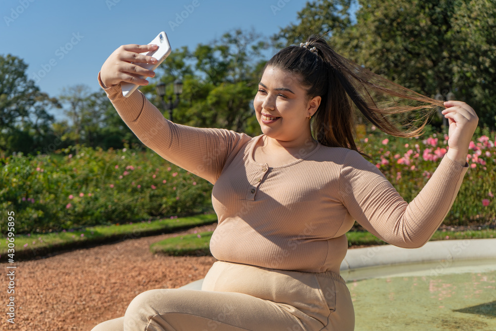 Beautiful young curvy girl taking a selfie while smiling happily outdoors. Beautiful young curvy girl taking a selfie while smiling happily outdoors.