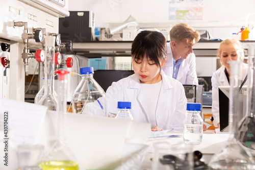Ordinary Chinese female student noting results of research at chemical lab