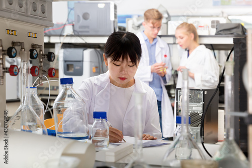 Casual Chinese female student noting results of research at chemical lab